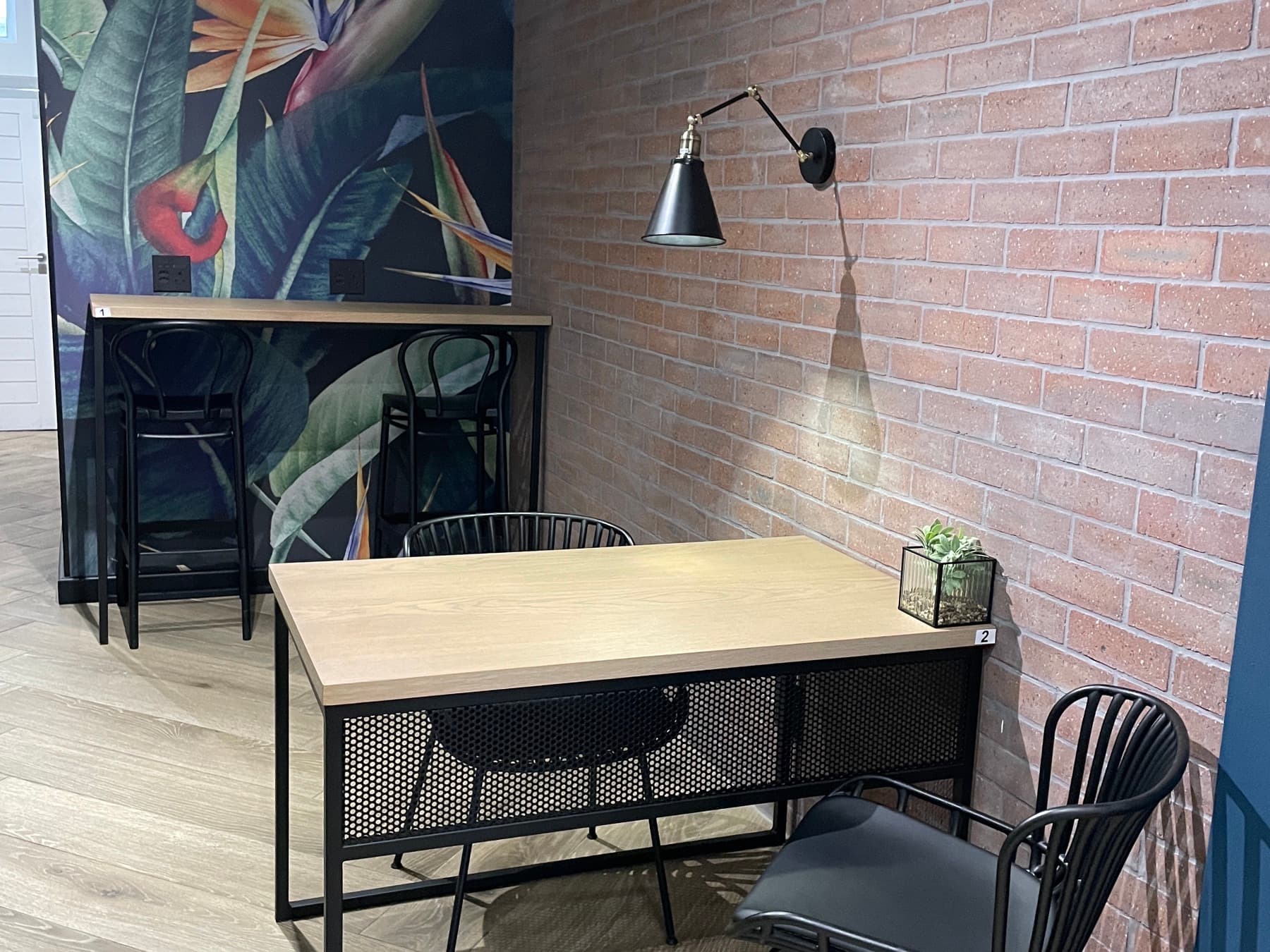 Dedicated work desks against the exposed brick wall in the SOHO work room, with a high table and the bird-of-paradise mural behind.