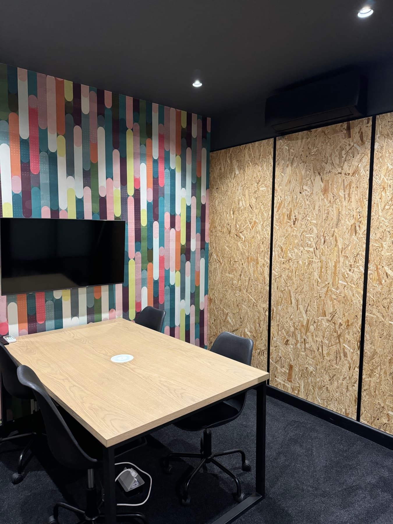 A SOHO private meeting room with a wall-mounted presentation screen and a colourful feature wall.