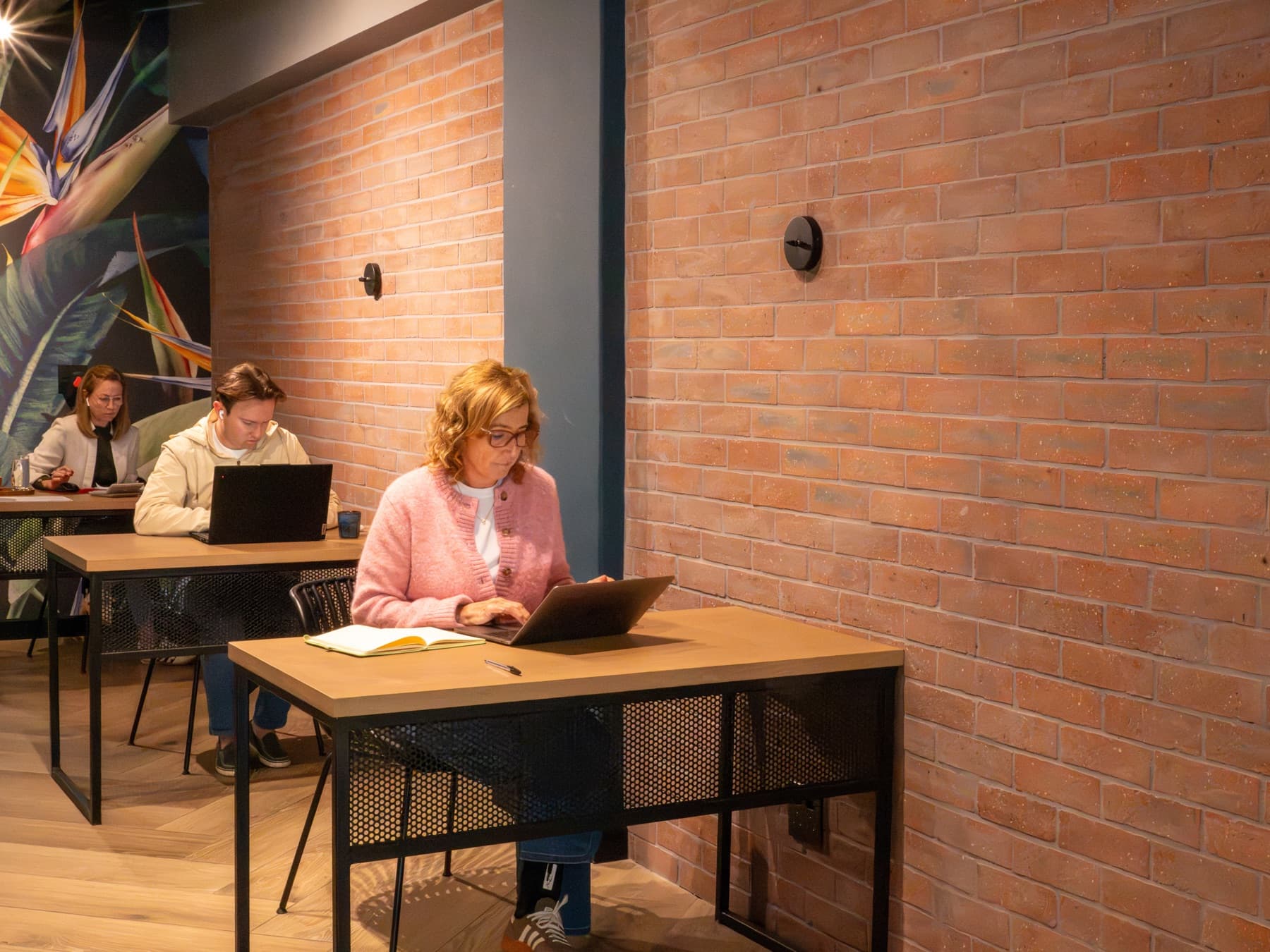 Three people working at separate desks along the exposed brick wall in the SOHO work space.